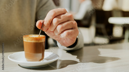 man stirs his machiatto with a coffee spoon photo