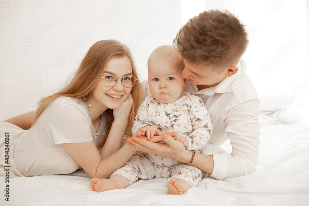 Happy joyful satisfied family of woman, man and infant baby lying in white bedspread. Family day, toddler development Happy joyful satisfied family of woman, man and infant baby lying in white bedspread. Family day, toddler development