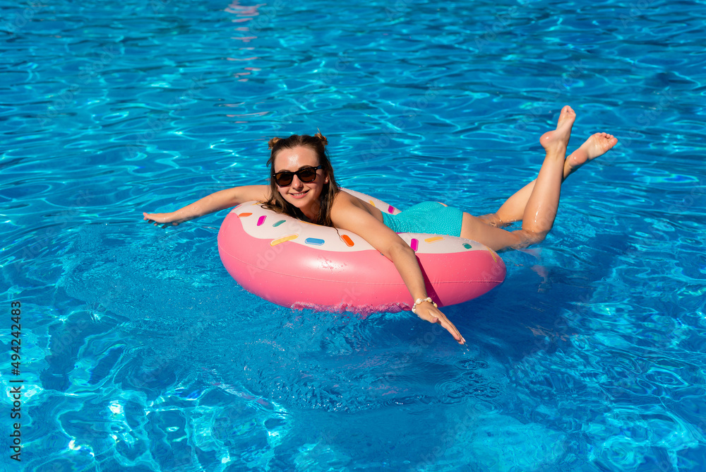 young girl in bikini swims on the inflatable water donut in the swimming pool