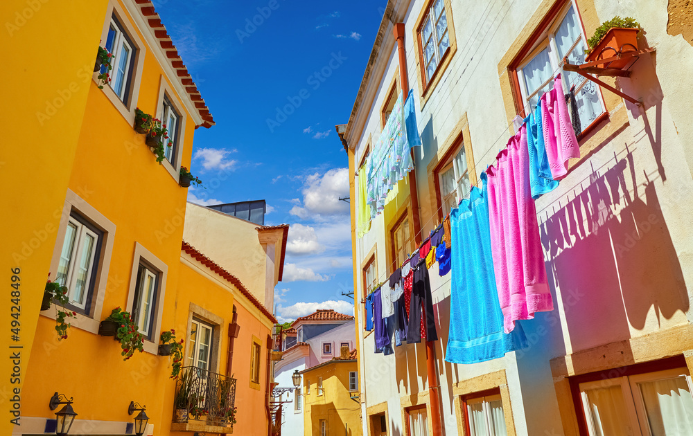 Lisbon, Portugal. Antique Alfama district with coloured houses on background of blue sky with clouds. Washed linen dry on ropes on streets between building. Decorative street lamp on the wall.