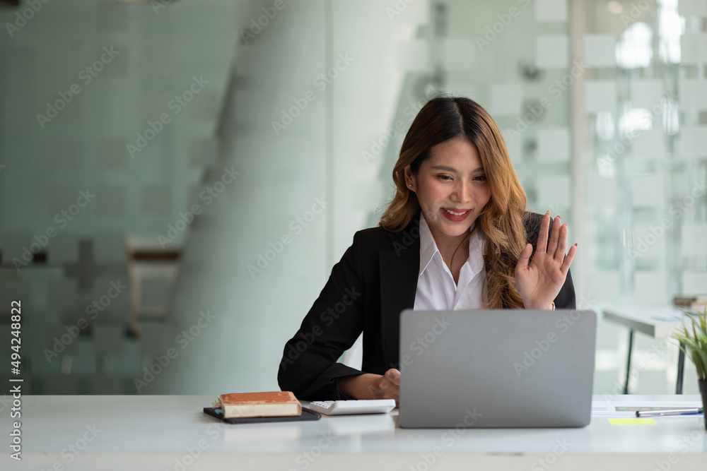 Portrait of smiling asian woman waving hello talking on video call. Successful young woman sitting white suits. Business conference via laptop Portrait of smiling asian woman waving hello talking on video call. Successful young woman sitting white suits. Business conference via laptop