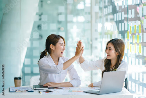Obraz na plátně Young asian business woman giving high five with friends while working with computer laptop at office
