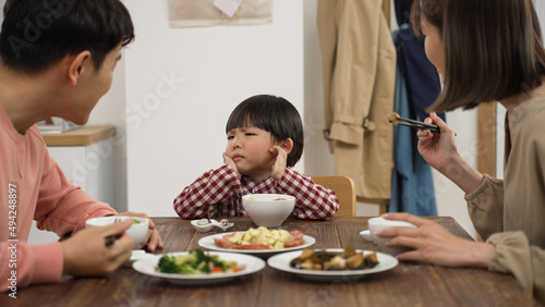 picky Asian boy shaking head while refusing food his father and mother put in his bowl during lunch time in dining room at home photo