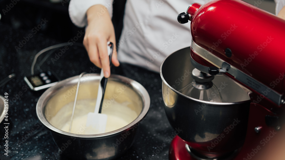 Closeup of chef stirring mixing cream in bowl while standing in the kitchen. Cake making, pastry production, dessert concept