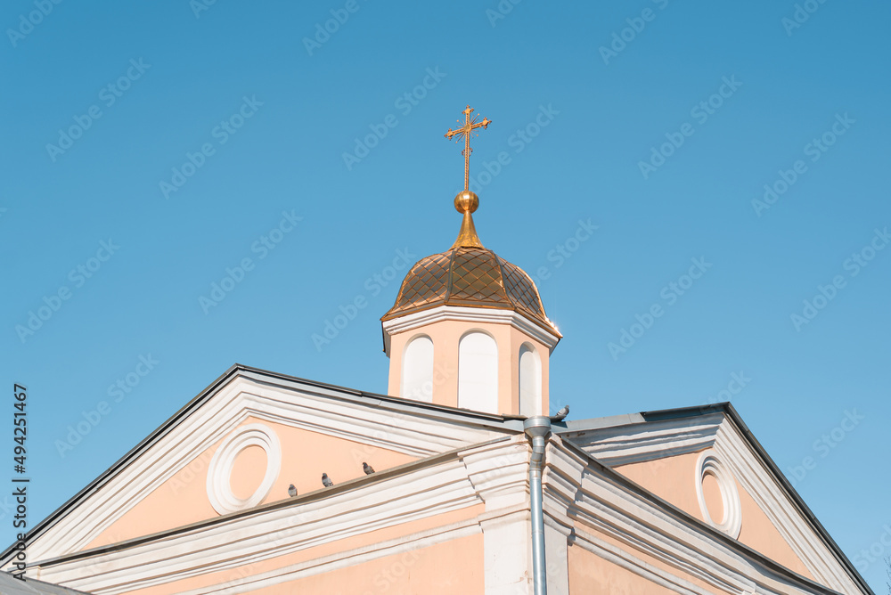 Church with golden dome and cross against clear blue sky. Exterior of an ancient religious building outdoors. Faith and religion concept