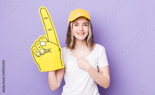 pretty caucasian woman smiling cheerfully, feeling happy and pointing to the side. number one fan hand