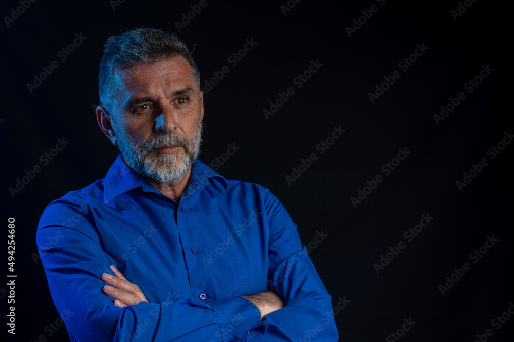 Portrait of an attractive mature bearded man in black studio. Strict male portrait. Dramatic portrait of a man in a low key with blue neon light. low key photo concept. Portrait of an attractive mature bearded man in black studio. Strict male portrait. Dramatic portrait of a man in a low key with blue neon light. low key photo concept.