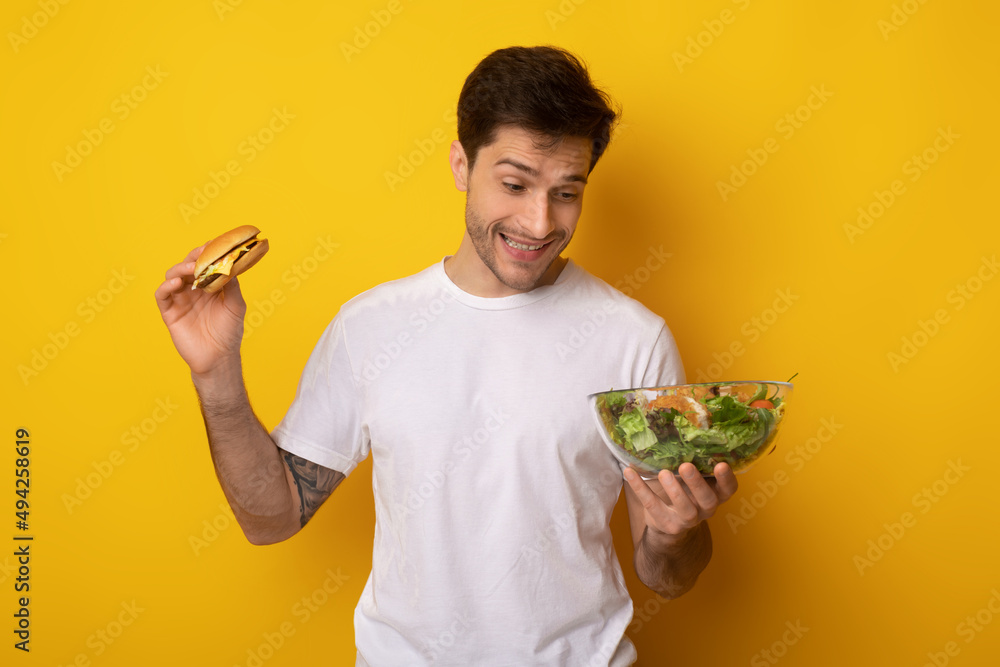 Portrait of Funny Young Guy Holding Burger And Salad Portrait of Funny Young Guy Holding Burger And Salad