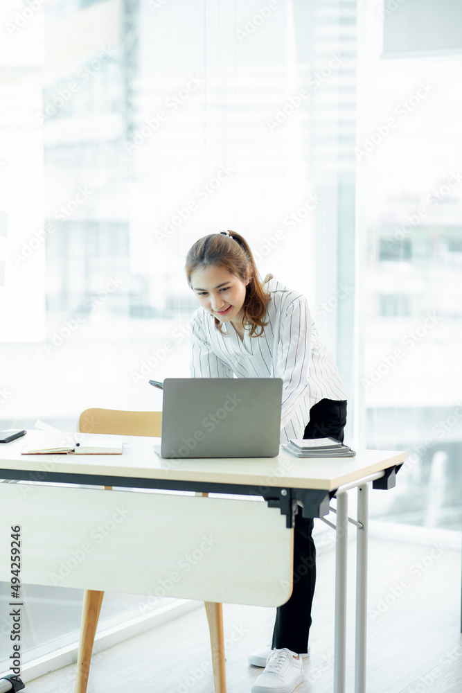 Excited Asian young woman using phone and laptop sitting on a desk office in the day at office Excited Asian young woman using phone and laptop sitting on a desk office in the day at office