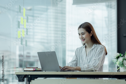 Cropped image of professional Asian businesswoman working at her office via laptop, young female manager using portable computer device while sitting at modern loft, flare light, work process concept