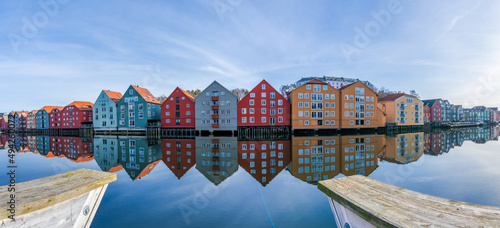 Wide panoramic view of old colorful wooden houses with reflections in river Nidelva in the Brygge district in Trondheim, Norway © beataaldridge