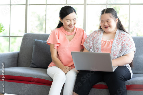 mother using laptop computer and a girl with down syndrome or her daughter, smiling and enjoying on sofa