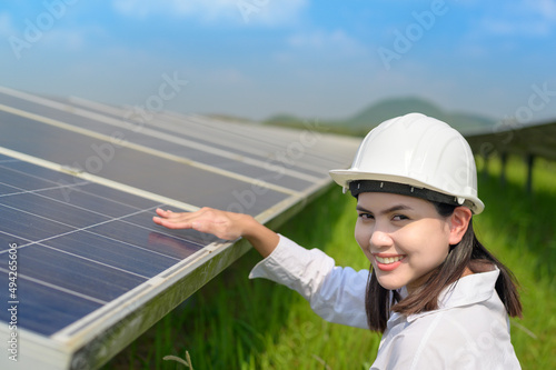 Female engineer wearing helmet in Photovoltaic Cell Farm or Solar Panels Field, eco friendly and clean energy.