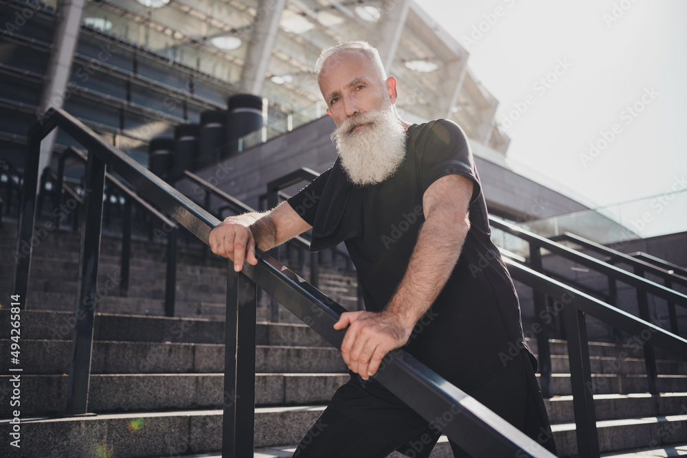 Portrait of attractive virile sportive healthy grey-haired man sportsperson standing on stairs fresh air spending time outdoors