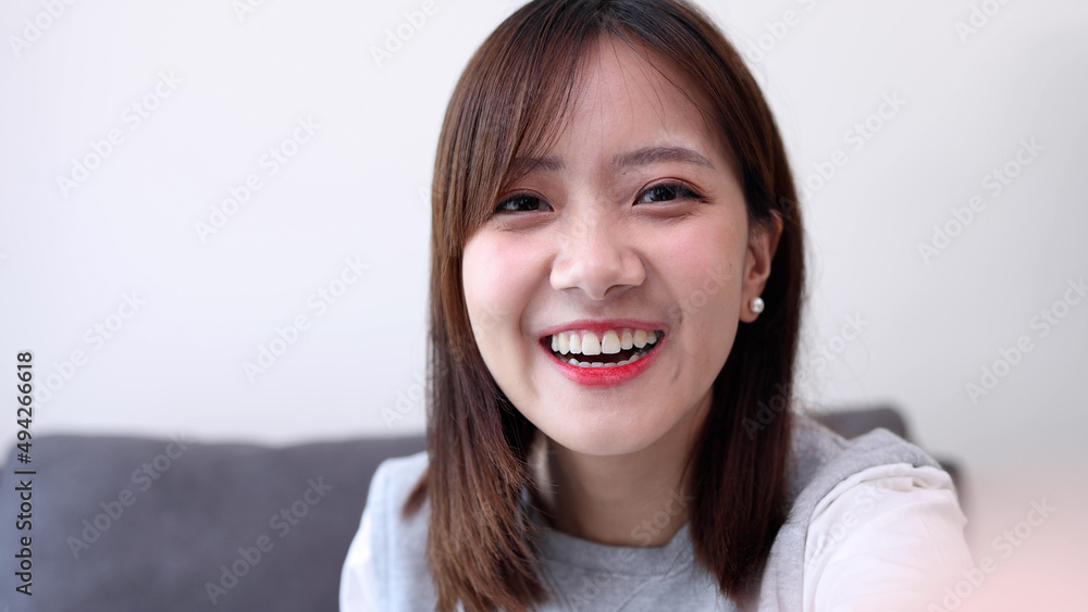 Young Asian woman making a video call smiling and talking with her friend and looking at camera on webcam application on mobile phone