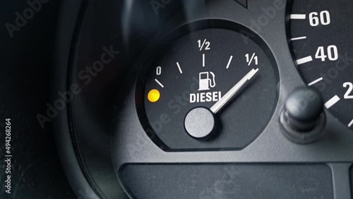Close-up shot of a diesel fuel gauge in a car. Yellow light indicator and meter pointer showing that the tank is empty. Glare of light present on the gauge glass cover. Copy space. 25fps