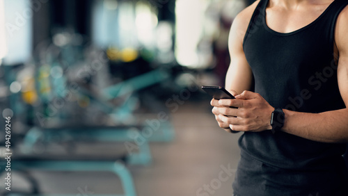 Cropped Shot Of Muscular Man Wearing Smartwatch Using Smartphone At Gym