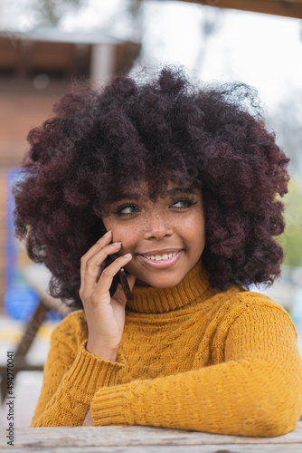 Young Afro woman on a phone call with her cell phone outdoors. The concept of an African American person answering her friends and sharing all her experiences with them.