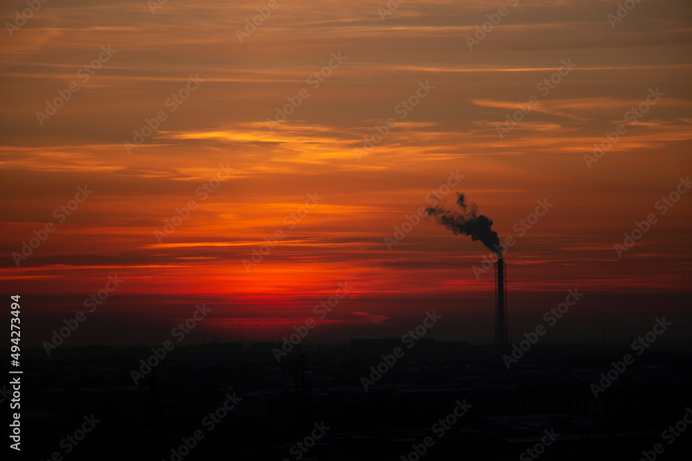 Red-orange sky. Pipe from the factory with smoke. Silhouette