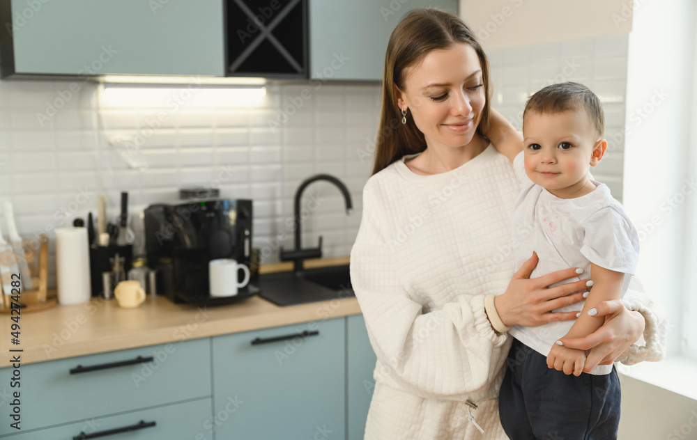 Happy mom and cheerful baby in the kitchen. Mother's love. Motherhood. The child is restless. Happy mom and cheerful baby in the kitchen. Mother's love. Motherhood. The child is restless.
