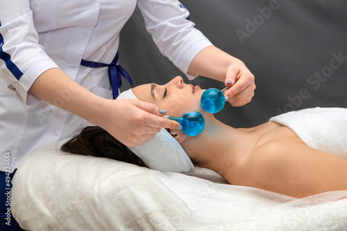 Cosmetologist uses glass massage balls for facial massage.Cosmetologist in the process of working with a client.A young woman enjoys cosmetic procedures while lying on a medical couch.
