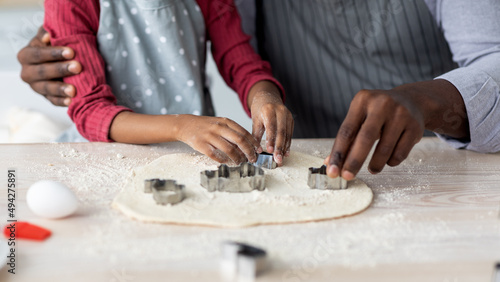 Hands of black man and child cutting dough for cookies
