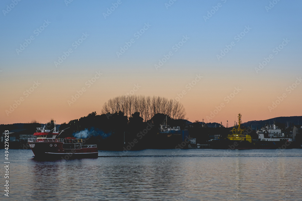 Beautiful sunrise over the lake with red boat and forest silhouette in the back, Valdivia, Chile