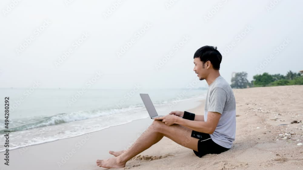 4K 50fps, Handsome Asian guy, video call meeting, job presentation with supervisor on a laptop computer, on the seashore where the waves hit him gently, comfortably, work from home. 4K 50fps, Handsome Asian guy, video call meeting, job presentation with supervisor on a laptop computer, on the seashore where the waves hit him gently, comfortably, work from home.
