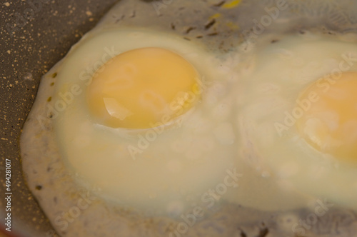 fried eggs in cast iron frying pan sprinkled with ground black pepper on wood table