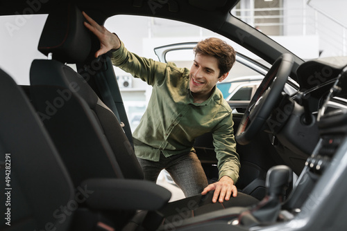 Happy young man looking inside car salon, selecting new automobile at modern dealership