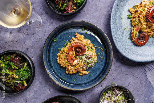 Fototapeta Naklejka Na Ścianę i Meble -  A portion of risotto with octopus tentacles. purple background. Top view