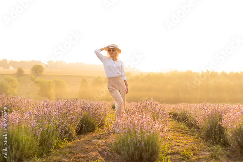 Fototapeta Naklejka Na Ścianę i Meble -  Young blond woman traveller wearing straw hat in lavender field surrounded with lavender flowers.