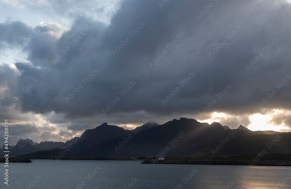 a small white car against the background of mountains on the coast of the northern sea in the rays of the evening sun, van life concept