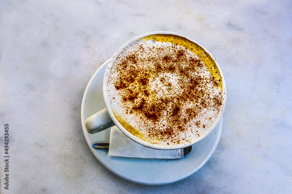 Frothy latte coffee with cinnamon sprinkles in white cup and saucer sitting on white marble table - top view and copy space Frothy latte coffee with cinnamon sprinkles in white cup and saucer sitting on white marble table - top view and copy space