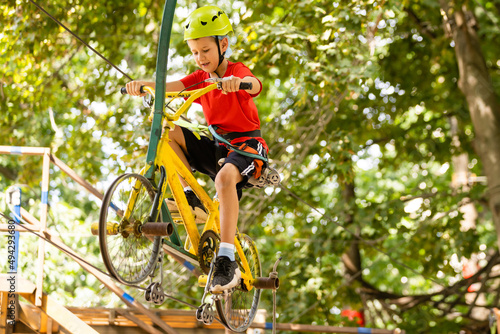 Adventure climbing high wire park - little boy on course in mountain helmet and safety equipment