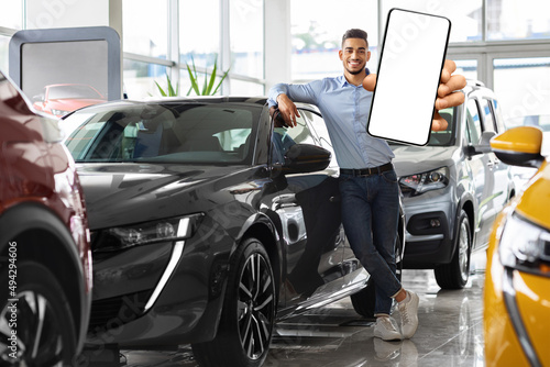 Wealthy middle eastern man posing next to car, showing smartphone © Prostock-studio