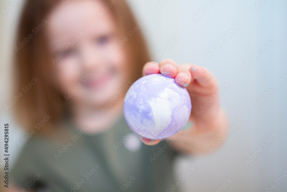 An Easter purple egg in focus in the hands of a little girl. Creative Easter. Selective focus An Easter purple egg in focus in the hands of a little girl. Creative Easter. Selective focus