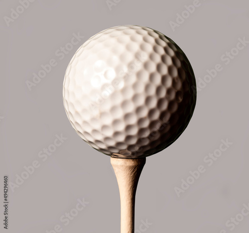 White golf ball on a tee, isolated on a grey background.