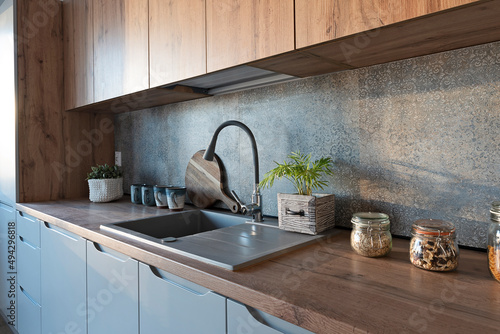 Modern kitchen interior with kitchen sink with stylish faucet, wooden counter and cabinets and tile pattern on the wall. Cozy home and new apartment.