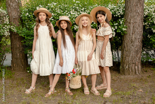 Smiling preteen girls standing near green blooming bush with basket of flowers