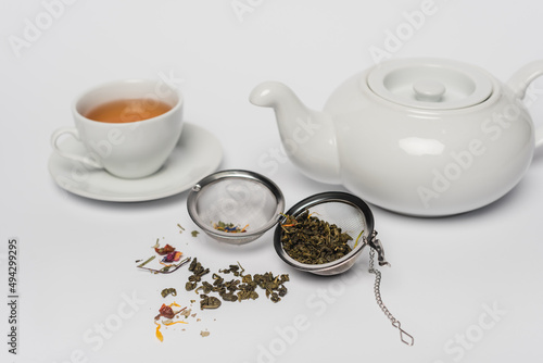 Dry tea in infuser near cup and teapot on white background. photo