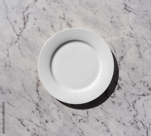 Food background concept - high angle view of white plate on grey marble textured bench with hard shadow from sunlight