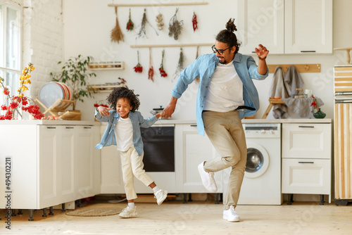 Happy african american family father and little son dancing to music in modern kitchen at home