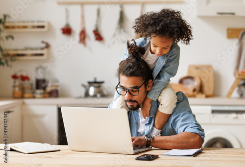 Modern ethnic busy man working remotely at home with playful kid photo