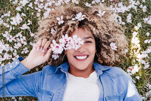 top view of happy hispanic woman with afro hair lying on grass among pink blossom flowers.Springtime