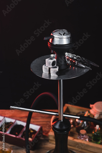 Hookah with coals near blurred dry tea isolated on black.