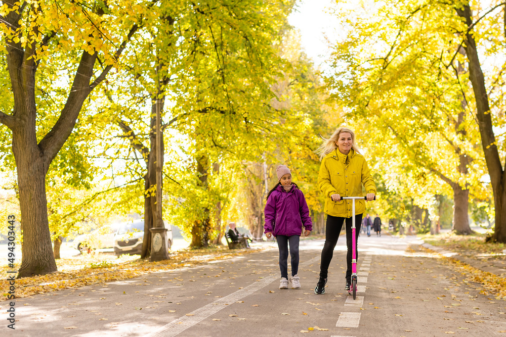 Mother and daughter are walking in the autumn in the park. woman is riding a scooter Mother and daughter are walking in the autumn in the park. woman is riding a scooter