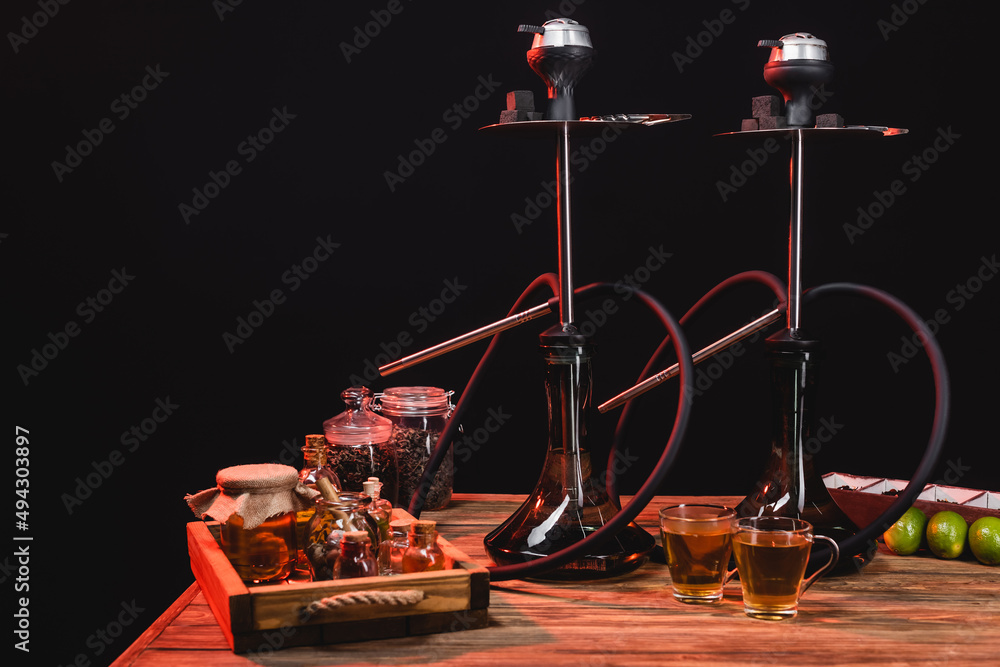 Tea cups near hookahs and limes on wooden surface isolated on black. Tea cups near hookahs and limes on wooden surface isolated on black.