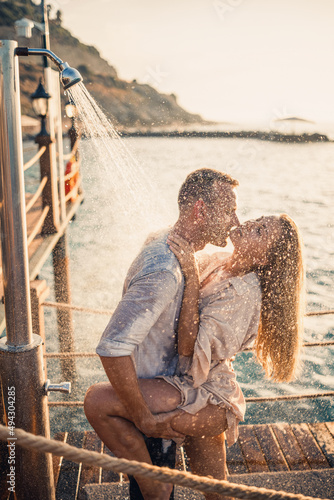 Happy couple by the sea. A guy and a girl are under the shower on an open-air pier. Happy couple on vacation. Man and woman by the sea.