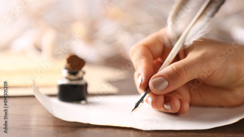 Woman writing in ink on paper sheet at table, closeup photo
